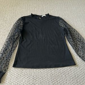 Black, high neck, puff-sleeved top. Sleeves are sheer with polka dots